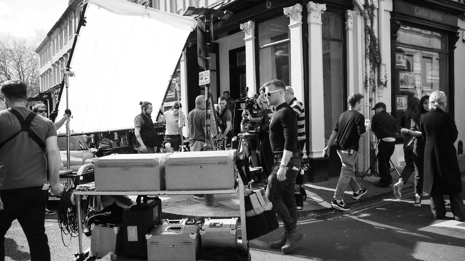 Large film crew working on a street location under a diffusion frame, black and white