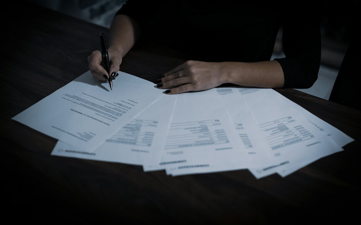 Hands signing documents spread across a dark desk